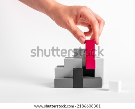 Woman assembling puzzle. Hand putting outstanding red element in black and white construction. Formation concept. Creative unique idea. Wooden logical toy. High quality photo
