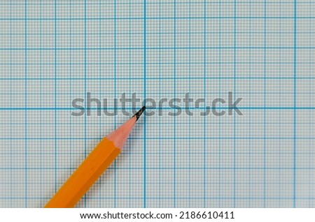 A simple graphite pencil on a blank sheet of a checkered notebook. School notebook with a pencil on the desktop. Take notes, space for text.