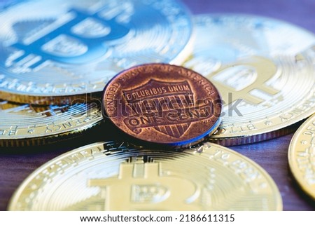 Golden Bitcoin coins and a US 1 cent coin on a wooden furniture in macro photography. Cryptocurrency, payment method and risk.
