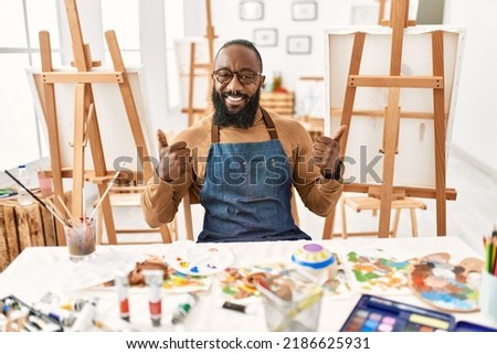 African american artist man at art studio success sign doing positive gesture with hand, thumbs up smiling and happy. cheerful expression and winner gesture. 