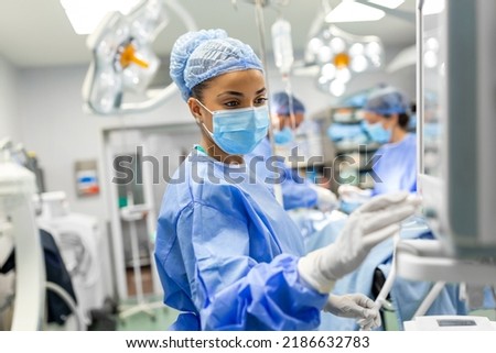Portrait of a young female doctor in scrubs and a protective face mask preparing an anesthesia machine before an operation Royalty-Free Stock Photo #2186632783