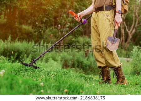 metal detector at work in the forest or field. Search for treasure and ancient values. Archeology. Man with a metal detector. Minesweeper Image