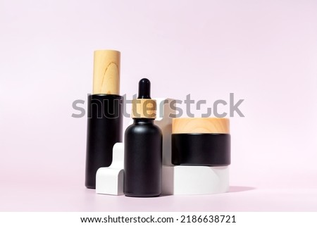 Set of black matte glass cosmetics bottles with bamboo lids on the white podium. Mockup background with cocncrete geometric figures and copy space. Stage with product presentation