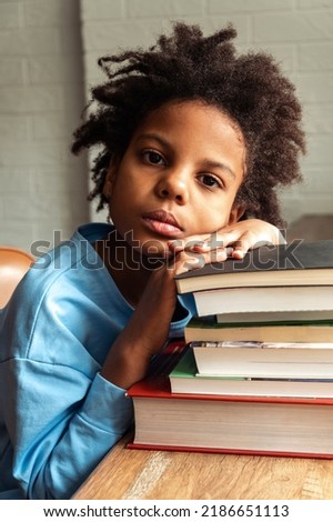 Sad tired African-American girl doing homework at home,puting her head on a stack of textbooks.Back to school concept.School distance education,home schooling,diverse people.