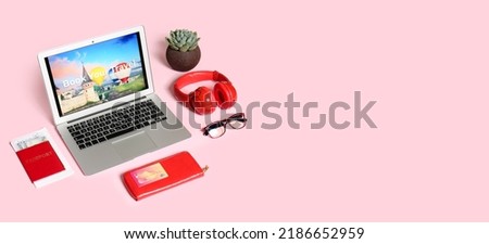 Open page of online booking service on screen of laptop and travel accessories on pink background with space for text