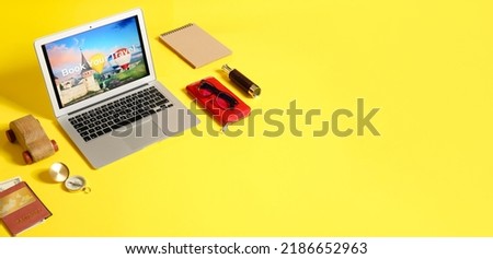 Open page of online booking service on screen of laptop and travel accessories on yellow background with space for text