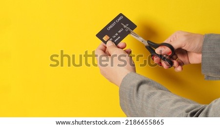 Hand is hold black credit card and scissors on yellow background. Man arm wear a grey suit