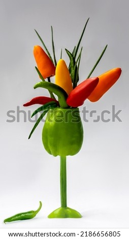 In a glass made of sweet peppers, a bouquet of mini peppers and green onions close-up on a white background.Edible composition.