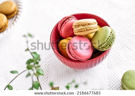 Colorful french macarons in pink bowl on white tablecloth. Tasty cakes macaroon of different colors. Strawberry, lime and lemon almond cookies, pastel colors.