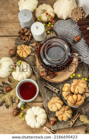 Autumn tea concept. Cookies with pumpkin puree, black tea in a glass teapot, fall decor. Wreath, candles, a cozy sweater. Old wooden background, top view