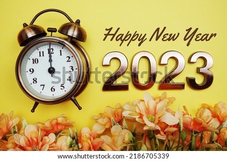 Happy New Year 2023 text with alarmclock and flower decoration on yellow background