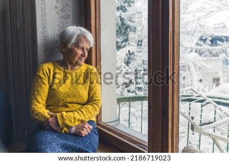 elder Caucasian woman sitting on the window-sill and looking outside cowboy shot indoor senior people concept. High quality photo
