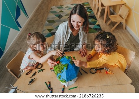 Natural science or Geography lesson at elementary school or kindergarten. Students playing with wild animals toys on handmade globe in the classroom. Selective focus. Royalty-Free Stock Photo #2186726235
