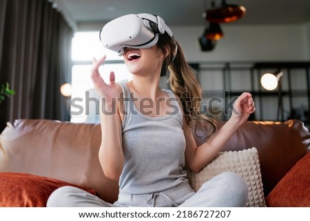 young attractive casual asian female woman watched the performance lives streaming concert in virtual reality through VR glasses goggle on sofa with fun and joyful moment in living room at home Royalty-Free Stock Photo #2186727207