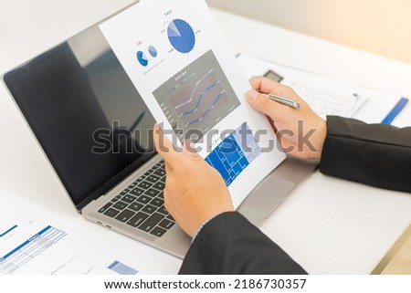 Businesswoman holding documents with financial statistics, stock photos, discussion and data analysis, charts and graphs with laptop computer. financial concept