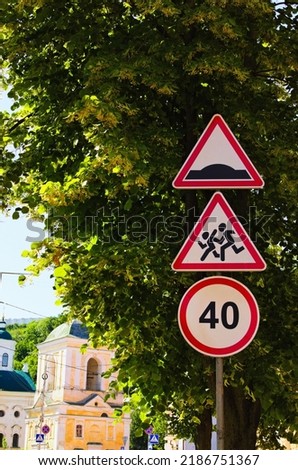 Traffic signs against green leaves linden tree at sunny morning. Warning Sign Children, Speed Limit Sign. Hump road sign post. Three road signs vertically on one pole. Blurred background. Royalty-Free Stock Photo #2186751367