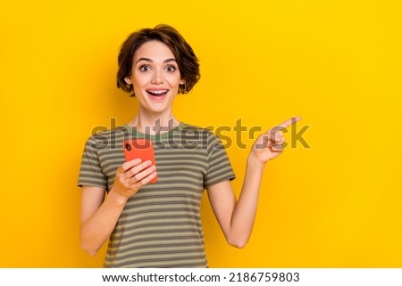 Photo of shiny excited lady wear striped t-shirt reading modern device pointing empty space isolated yellow color background