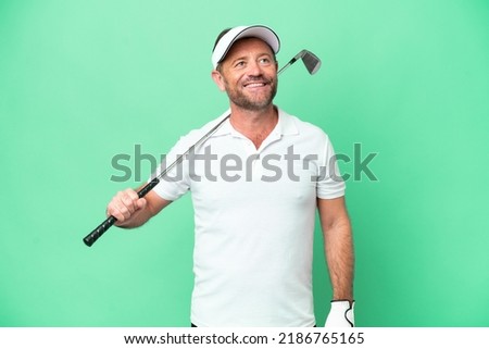 Middle age caucasian man isolated on green background playing golf and looking up while smiling