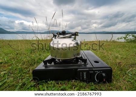 Camping gas stove with kettle on the background of mountains, grass and the shores of a reservoir or lake