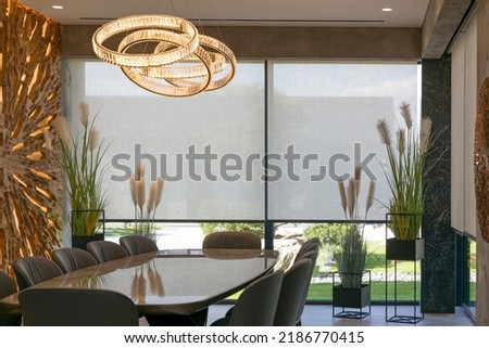 Roller blinds in the interior. Automatic solar shades large size on the window. Modern interior with wood decor panel on the wall. Green plants in hi-tech flower pots. Electric curtains for home.  Royalty-Free Stock Photo #2186770415