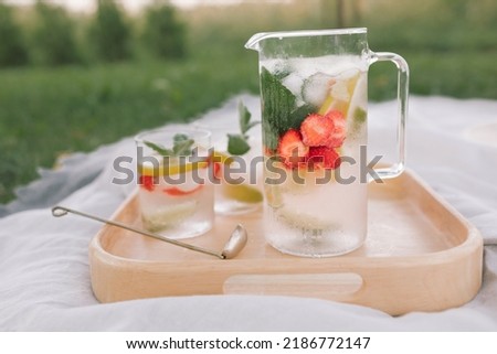 Summer non-alcoholic drinks with berries and mint on wooden tray in nature. Summer picnic in the countryside.