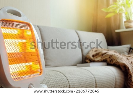 The electric portable heater is on in the room next to the couch. Royalty-Free Stock Photo #2186772845