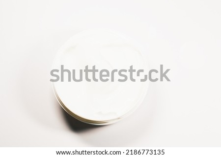 Moisturizing cream in an open plastic jar small on a white background. Flat lay, top view.