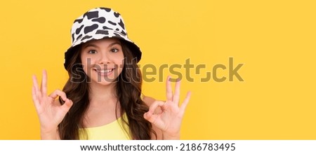 happy kid in summer bucket hat has curly hair on yellow background, ok. Child face, horizontal poster, teenager girl isolated portrait, banner with copy space.