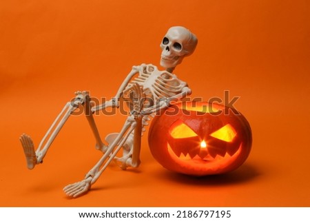 Halloween pumpkin head jack lantern with burning candles and skeleton on orange background. Creative halloween still life