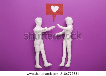 Valentine's day or halloween concept. Two mummy dolls wrapped in bandages with a like icon on a purple background