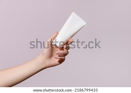 Hand holds blank white plastic tube on pink background. Cosmetic beauty product branding mock-up. Copy space. High quality photo Royalty-Free Stock Photo #2186799433