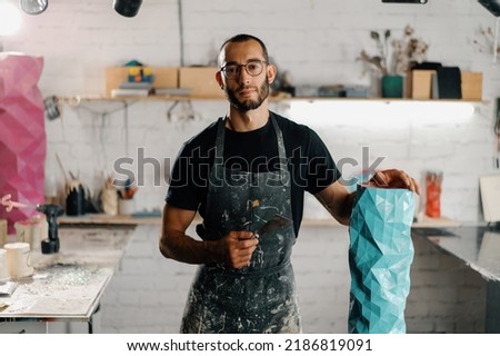 Artisan sculptor artist of Arab appearance smiling at camera against backdrop of the workshop and his product Royalty-Free Stock Photo #2186819091