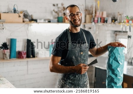 Artisan sculptor artist of Arab appearance smiling at the camera against the backdrop of workshop and his product Royalty-Free Stock Photo #2186819165