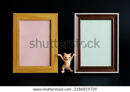 Two blank empty frames for pictures, photos or ads. Next to a funny toy dancing cat . Black background. A memorable element of the interior. Сopy space. Close-up