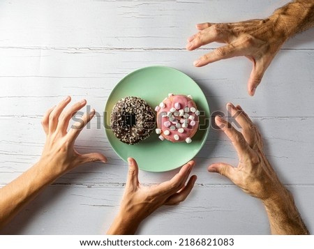 Unrecognizable people pick up a donut from a plate on a wooden table. Top view of the placement in plan