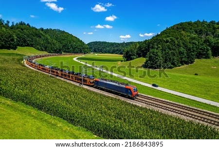 A freight train transports cars through the green valley in summer. Train ride on railway track. Train on railroad. Railroad train scene Royalty-Free Stock Photo #2186843895