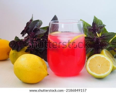 Basil lemonade. A pink drink in a glass is surrounded by fresh basil and lemons. Bright composition on a white background.