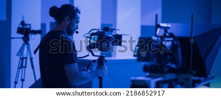 Director of photography with a camera in his hands on the set. Professional videographer at work on filming a movie, commercial or TV series. Filming process indoors, studio Royalty-Free Stock Photo #2186852917