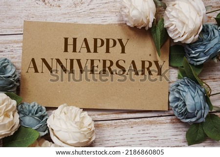 Happy Anniversary written on paper card and rose flower bouquet on wooden background