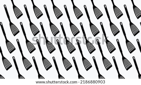 Pattern of black plastic turner spatula on white background.