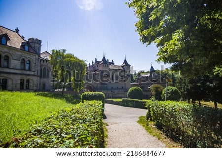 Photo of lichtenstein castle or Schloss on forested rock cliff in Swabian Alps in summer. Seasonal panorama of romantic fairytale palace in Gothic revival style over sky. European famous landmark