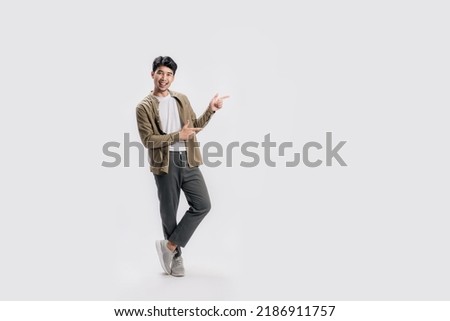 Full length smart young Asian man happy smile standing hand pointing to empty space on white background. Short on studio. Royalty-Free Stock Photo #2186911757