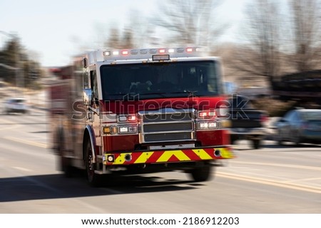 Motion panned view of a fire truck racing with sirens blaring to the scene of an emergency. Royalty-Free Stock Photo #2186912203