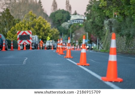 Bright orange road cones reduce street lanes while workers trim edge