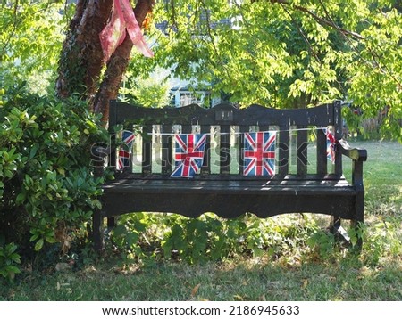 Union jack UK flag bunting on a wooden  bench on grass with trees and side and  background.      