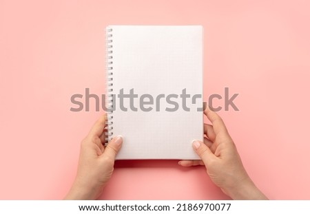 Notepad mockup. female hands holding blank spiral notepad or calendar over pink table background. hands shows open notebook. Female hands holding blank white notebook. copy space Royalty-Free Stock Photo #2186970077