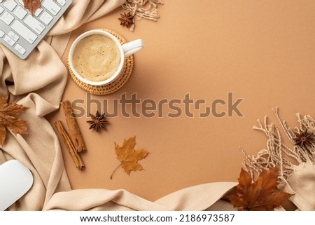 Autumn business concept. Top view photo of cup of frothy cocoa on rattan serving mat computer mouse keyboard yellow maple leaves cinnamon sticks anise and plaid on isolated beige background