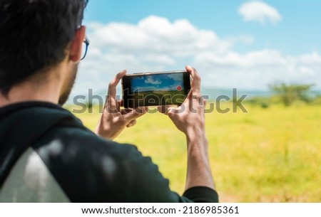 Rear view of a person taking a photo of a field with his cell phone, rear view of a man taking photos of a field, Close up of tourist man taking photos of a landscape.
