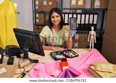 Young hispanic woman holding dataphone at retail business looking positive and happy standing and smiling with a confident smile showing teeth 