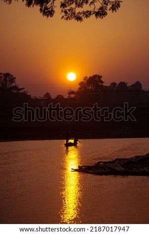 A vertical shot of sunset with reflection in the water and a small boat with people
